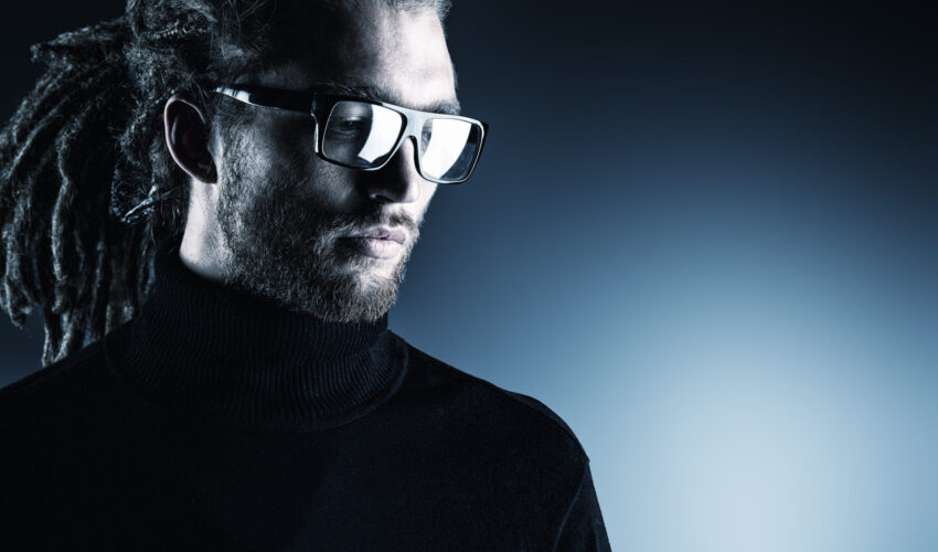 Portrait of a modern handsome young man in spectacles over dark background.